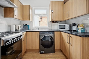 Kitchen area with washing machine, stove, microwave, and coffee maker.