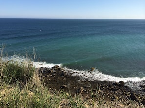 A rocky shoreline with waves crashing onto the beach and a clear view of the ocean.