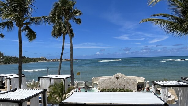 Um hotel à beira-mar com cabanas brancas com dossel, área de piscina e vista para o oceano.