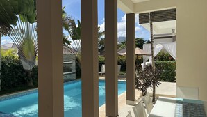 Uma área de piscina com borda em azulejo, cadeiras de descanso e uma estrutura de pérgola.
