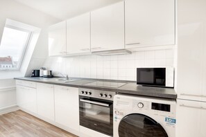 Una cocina moderna con armarios blancos, horno integrado, microondas y lavavajillas.