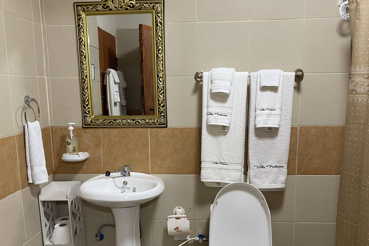 Ein Badezimmer mit Waschbecken, Toilette und Spiegel. Handtücher hängen an der Wand und ein Korb steht auf dem Boden.