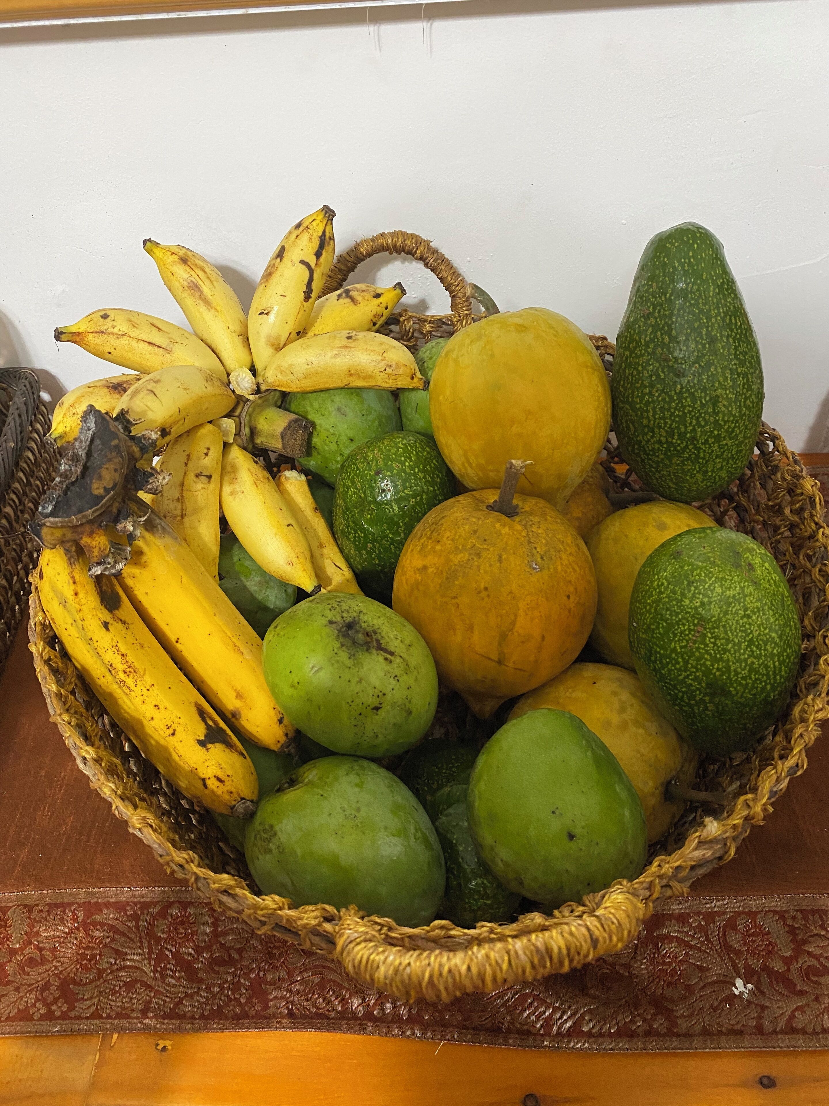 Una cesta de frutas con plátanos, aguacates y melones verdes y amarillos.