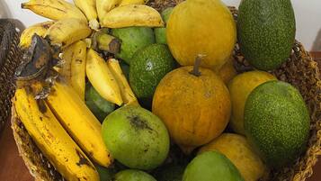 Una cesta de frutas con plátanos, aguacates y melones verdes y amarillos.