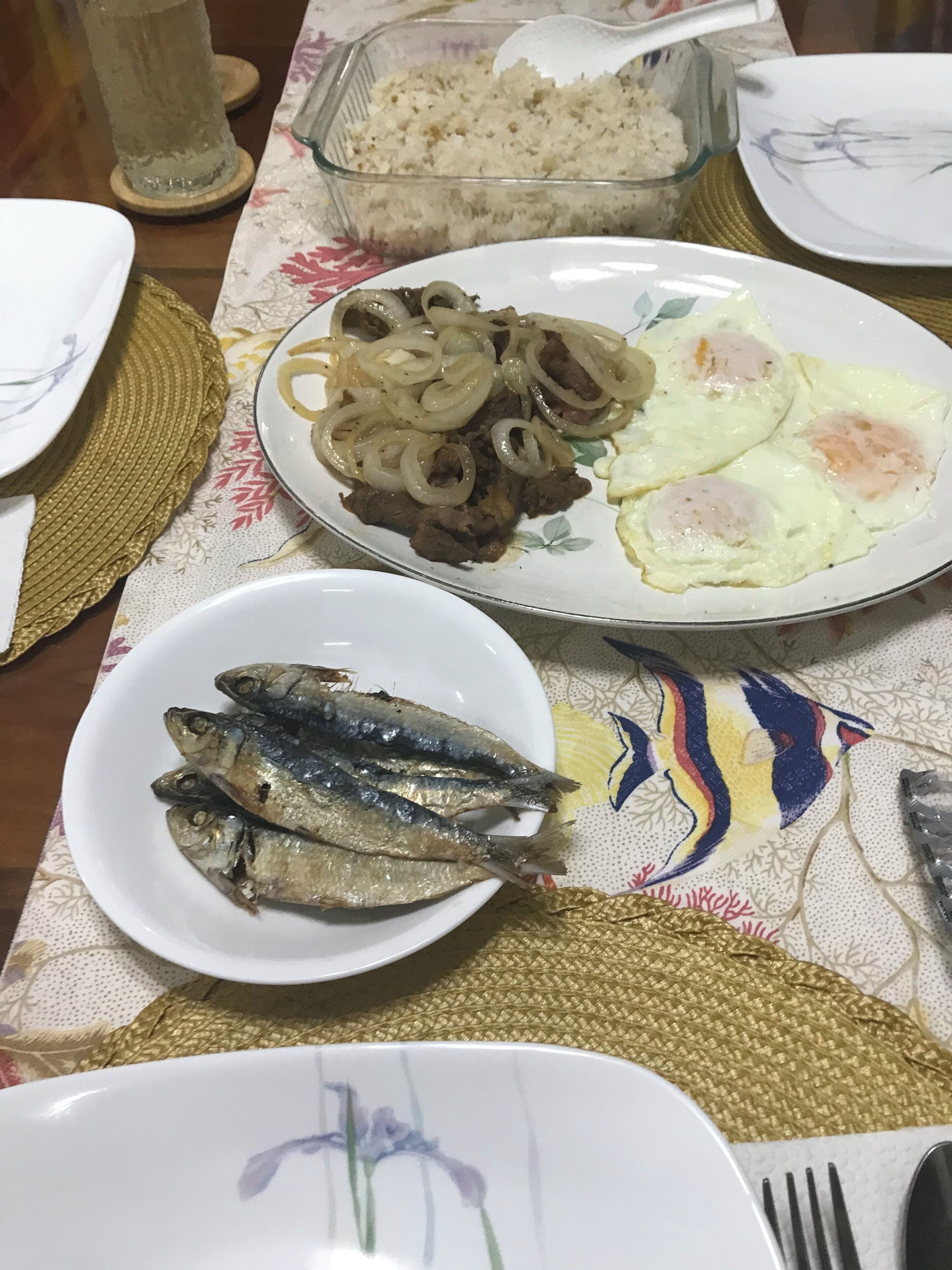 Una mesa de comedor con platos de comida, incluyendo huevos fritos, cebollas y pescado.
