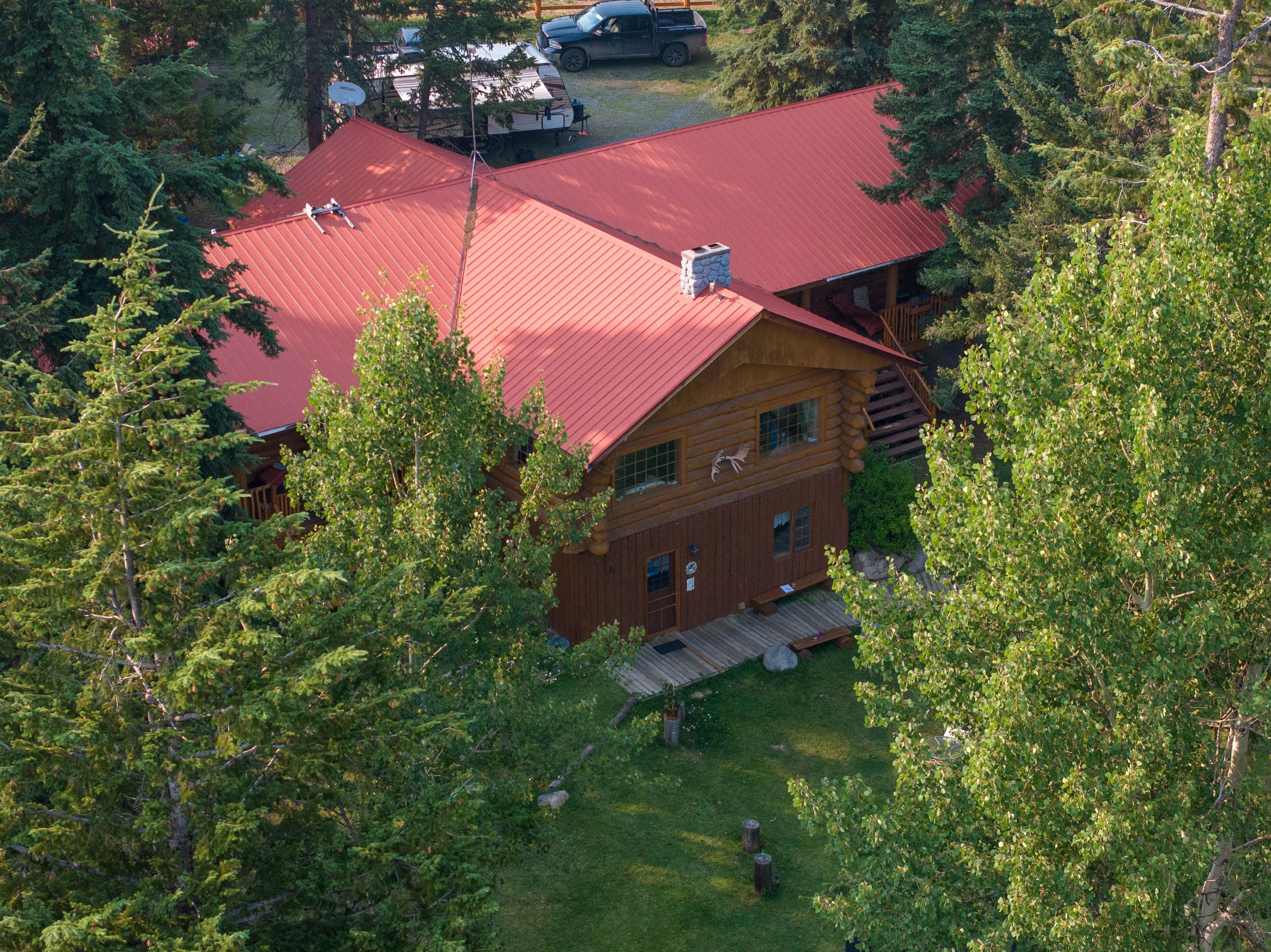 A log cabin with a red roof, surrounded by dense forest.