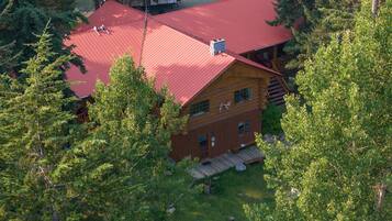 A log cabin with a red roof, surrounded by dense forest.