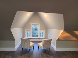 A room with a sloped ceiling, a large window with multiple panes, and two upholstered chairs.
