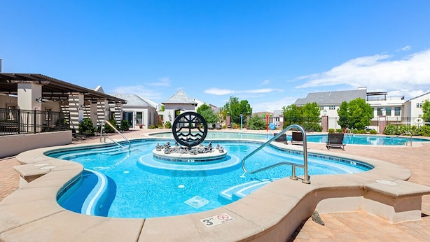 En swimmingpool med en central skulptur, omgivet af liggestole og et overdækket område med en pergola.