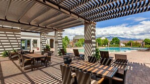 En udendørs patio med pool, overdækket siddeområde og bjergudsigt.