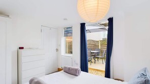 A bedroom with a bed, a window, and a view of an outdoor patio. - Coastal East View (St Helens)