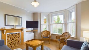 Ett vardagsrum med en öppen spis, en tv, flätade fåtöljer och en soffa.