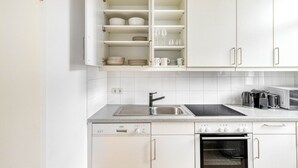 Una cocina moderna con armarios blancos, un lavamanos de acero inoxidable, horno integrado y microondas.