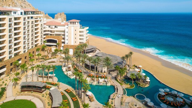 Ein Resort mit mehreren Schwimmbecken, einem Strand und einer Bergkulisse.