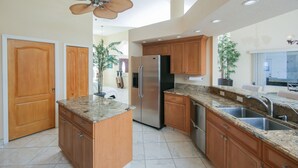 Une cuisine moderne avec des meubles en bois, des plans de travail en granit, un réfrigérateur en acier inoxydable et un ventilateur de plafond.