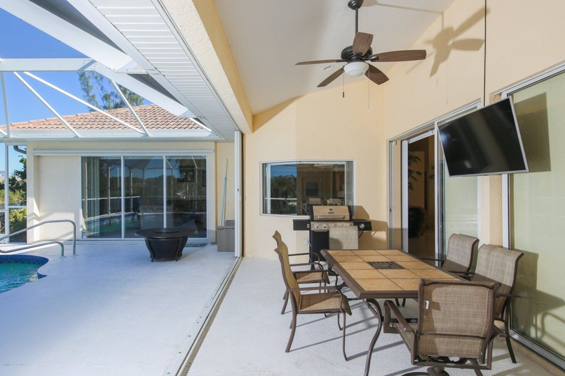 An outdoor patio with a table and chairs, a ceiling fan, a TV, and a pool.