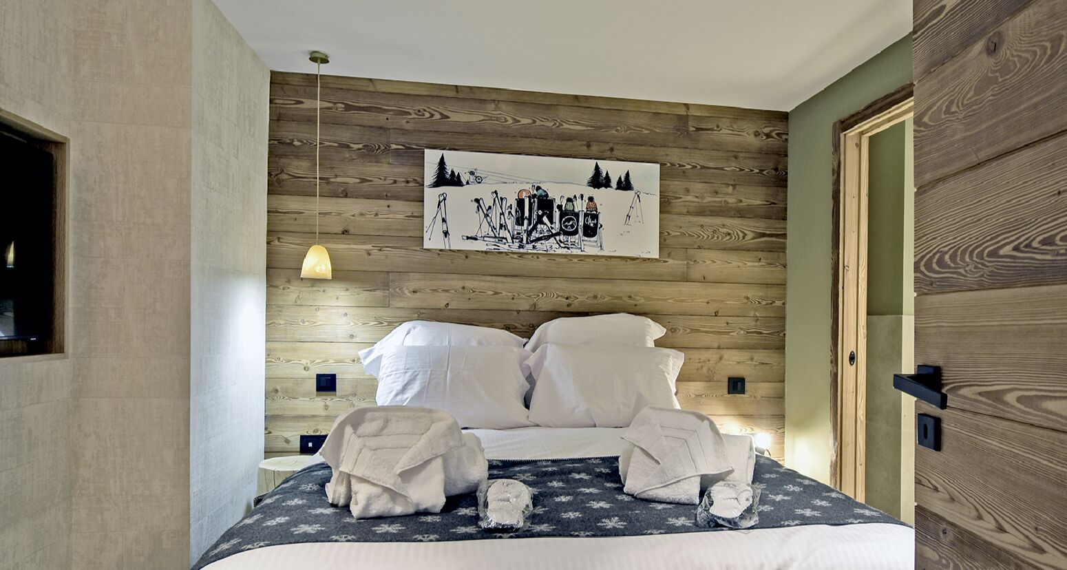 Une chambre d’hôtel avec une tête de lit en bois, un lit recouvert de draps blancs et un tableau représentant une scène de ski.