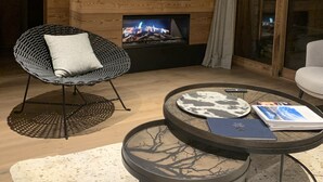 A modern living room with a fireplace, a television mounted on a wooden wall, and two chairs. - Magnificent 8-person Meribel Centre apartment with Nordic bath on terrace (Les Allues)