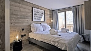 A bedroom with a wooden wall, a framed picture, a bedside lamp, and a bed with white bedding. - Magnificent 8-person Meribel Centre apartment with Nordic bath on terrace (Les Allues)