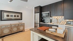A modern kitchen with dark cabinets, stainless steel appliances, and a wooden dining table with a cutting board and bowls. - 30A Perfect for 2-Private Beach-Tennis/ Pickle ball/Tesla Universal EV Charger (Santa Rosa Beach)