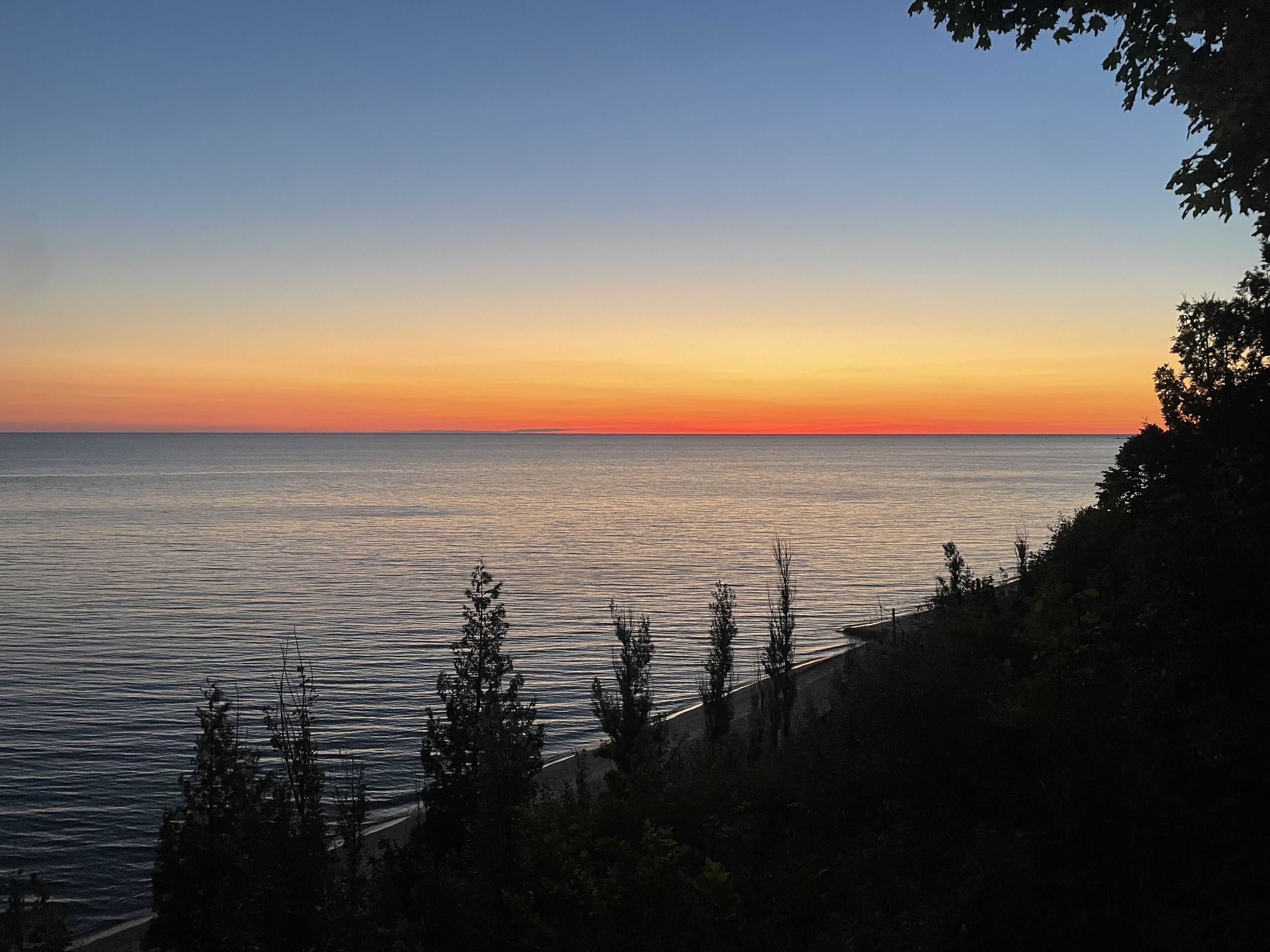 A coastal sunset view with calm waters and a rocky shoreline.
