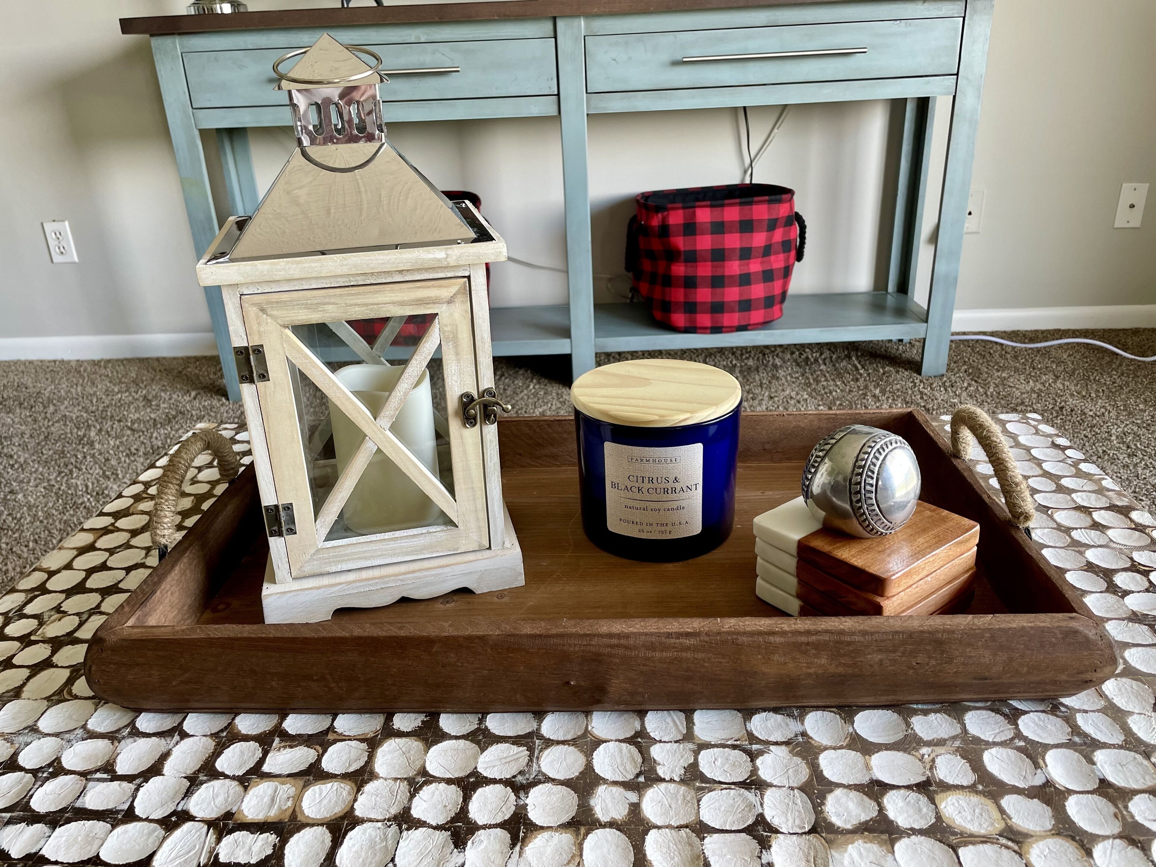 A wooden tray with a candle, a lantern, and a decorative item on a patterned carpet.
