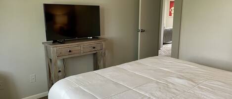 Un dormitorio con cama, televisor sobre un mueble de madera y una puerta que da a otra habitación.