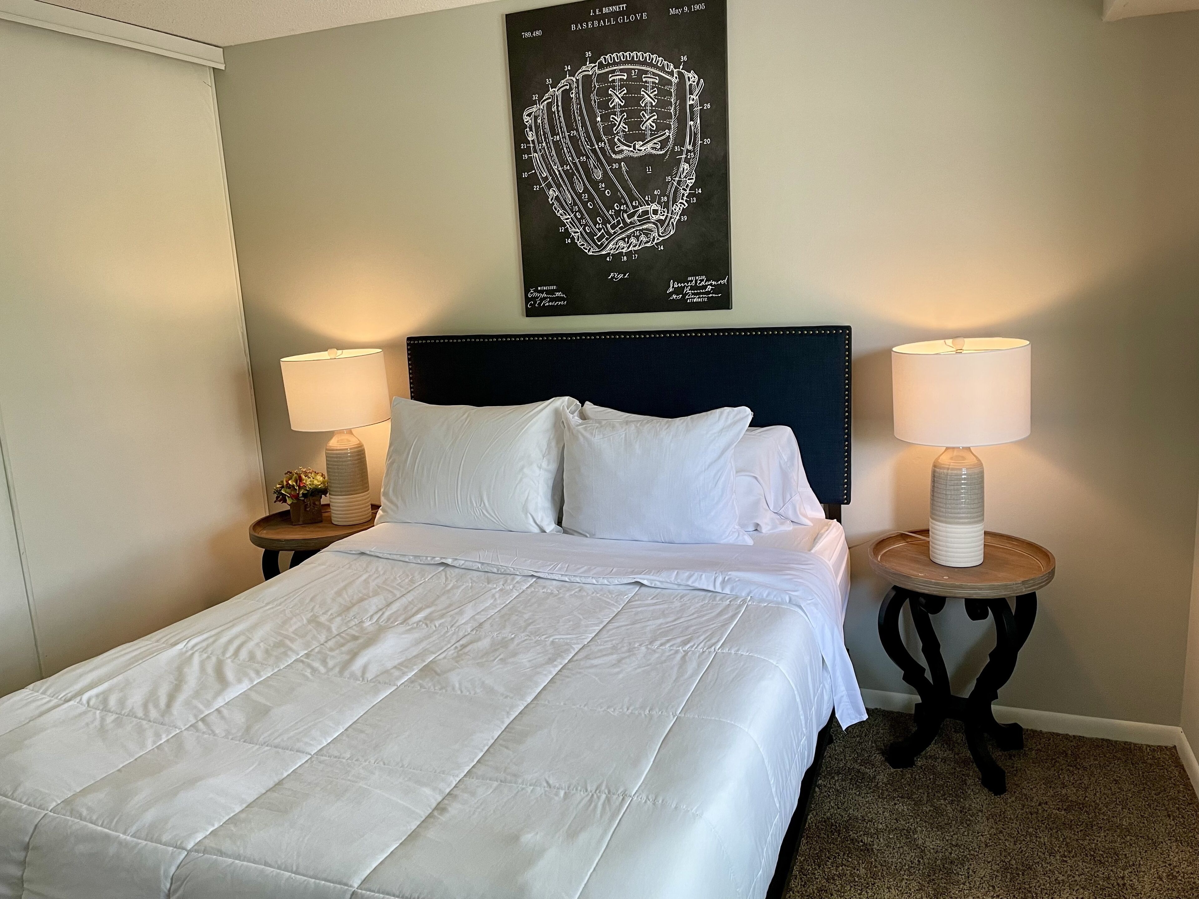 A neatly made bed with white linens, two bedside tables with lamps, and a wall-mounted artwork above the bed.