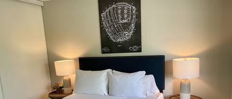 A neatly made bed with white linens, two bedside tables with lamps, and a wall-mounted artwork above the bed.
