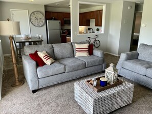 A living room with a grey sofa, a coffee table, and a kitchen in the background.