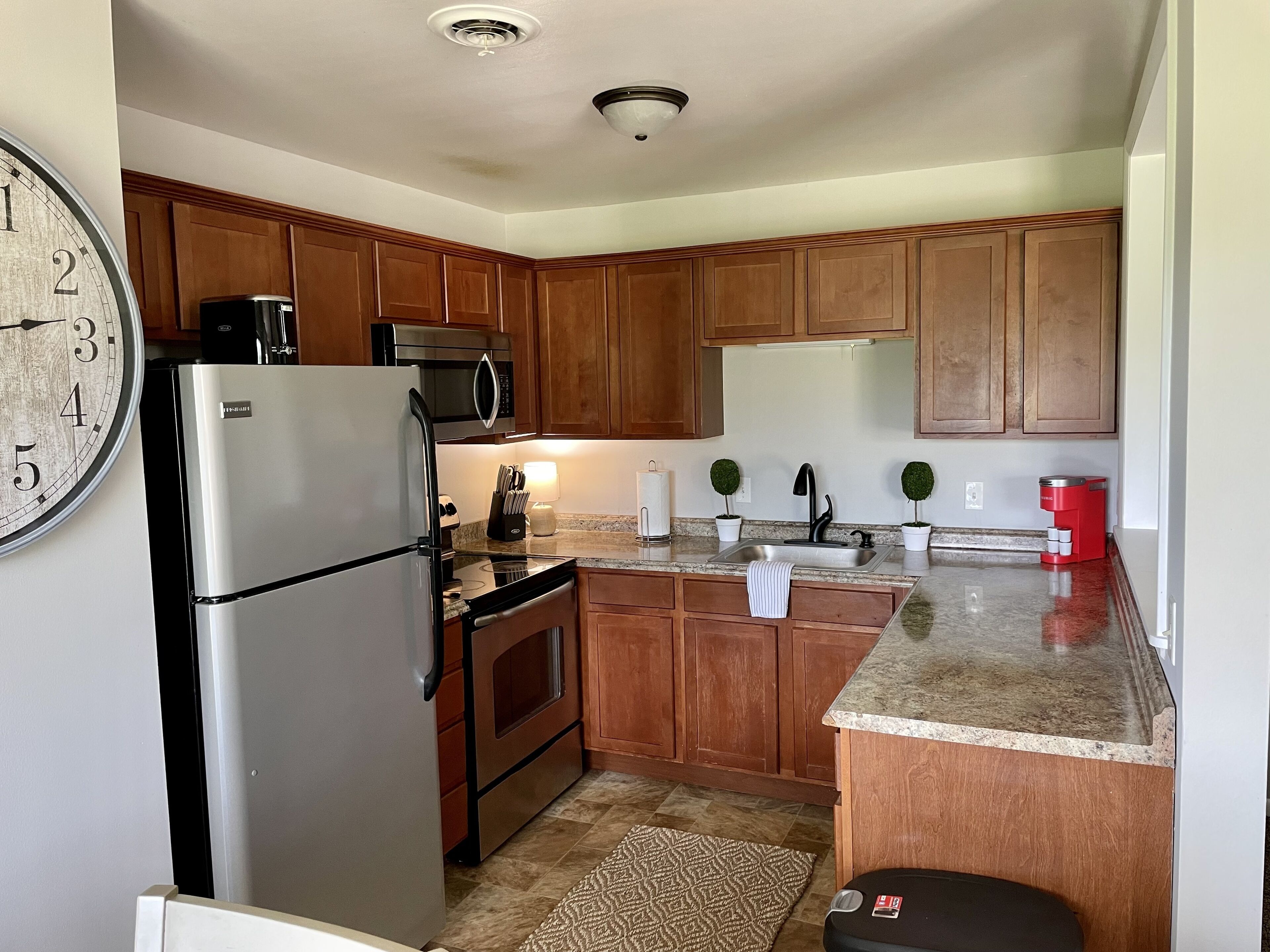 A kitchen with wooden cabinets, stainless steel appliances, a clock, and a coffee maker.