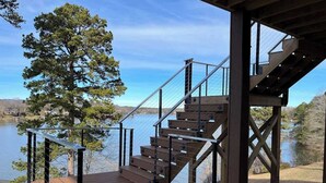 A wooden deck with a staircase leading to a covered area overlooking a body of water. - Modern Lakefront Views at Lake Hickory Haven (Hickory)