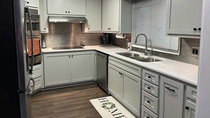 A modern kitchen with white cabinetry, stainless steel appliances, and a window with blinds. - Modern Lakefront Views at Lake Hickory Haven (Hickory)