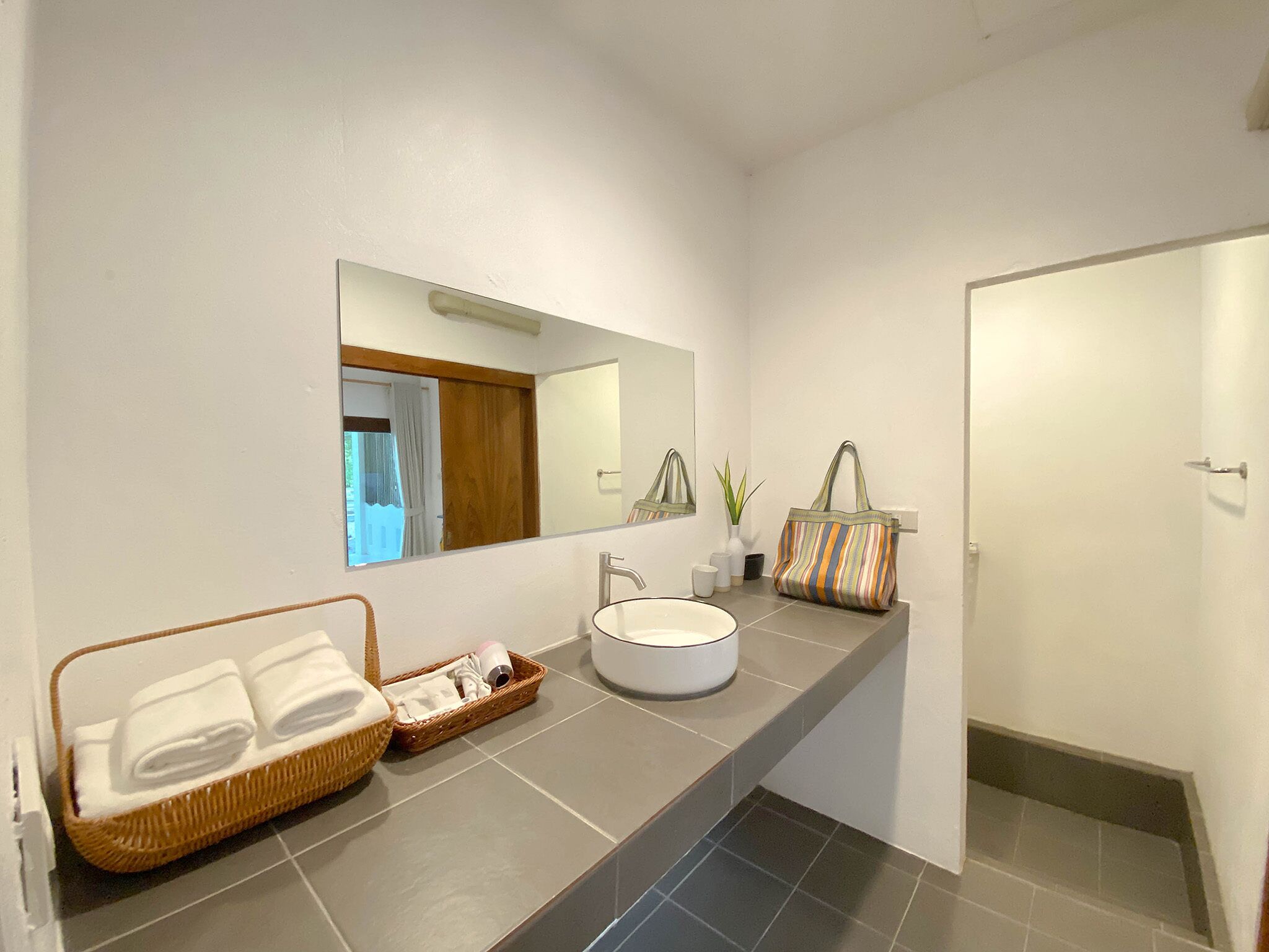 Un baño moderno con un espejo grande, un lavamanos y una cesta de mimbre con toallas.