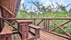 A wooden deck with a table and benches, surrounded by a metal railing, overlooking a forested area.