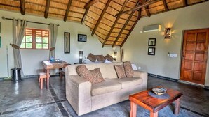 A spacious living area with a high ceiling, a sofa with patterned cushions, a wooden coffee table, and a dining table with chairs.
