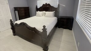 Un dormitorio con cama de madera, cómoda, mesita de noche, ventilador de techo y ventana con persianas.