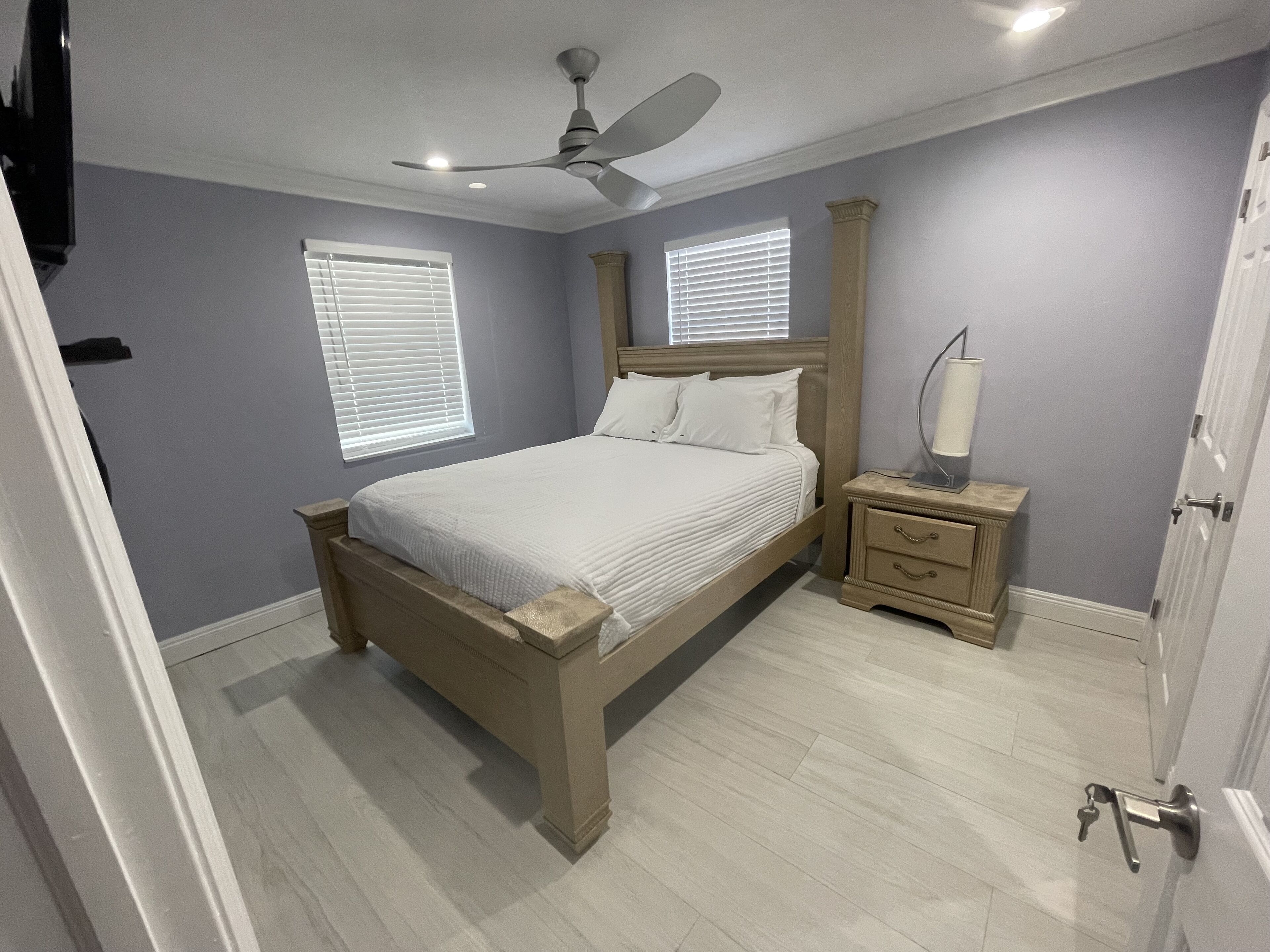 A bedroom with a bed, nightstands, a ceiling fan, and two windows with blinds.