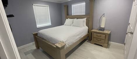 A bedroom with a bed, nightstands, a ceiling fan, and two windows with blinds.