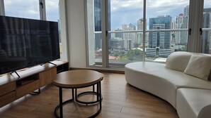 Una sala de estar moderna con un televisor grande, una mesa redonda, un sofá y vistas de la ciudad a través de amplios ventanales.