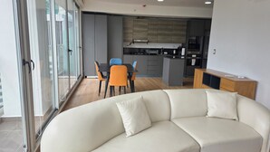 Una sala de estar moderna con un sofá blanco, un comedor con sillas naranjas y una cocina con armarios grises.