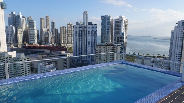 Una piscina infinita en la azotea con vistas al horizonte urbano, rodeada de edificios altos.