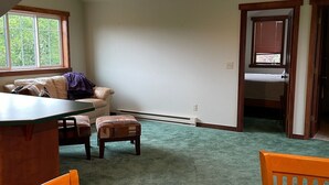 Ein geräumiges Zimmer mit hohen Decken, einem Esstisch mit Stühlen, einer Couch und einem Fenster.