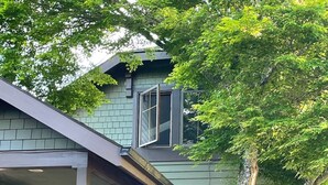 Ein zweistöckiges Haus mit Veranda, einem Baum und einem Ziegelkeller.