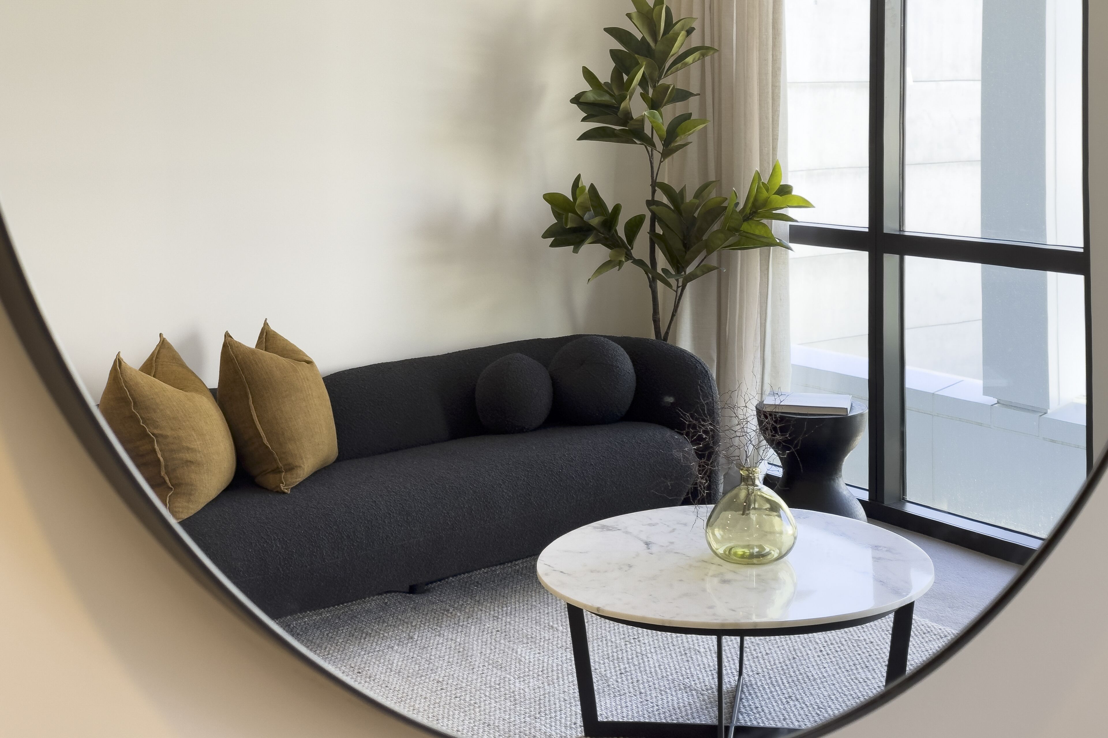 A modern living room with a dark gray sofa, three brown cushions, a white marble coffee table, and a potted plant.