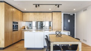 A modern kitchen with wooden cabinets, a central island, and a dining area with a wooden table and black chairs. - Modern tranquility in the city (Auckland)