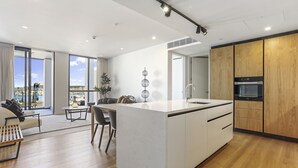 A modern kitchen with a central island, wooden cabinets, and a large window offering a city view. - Modern tranquility in the city (Auckland)