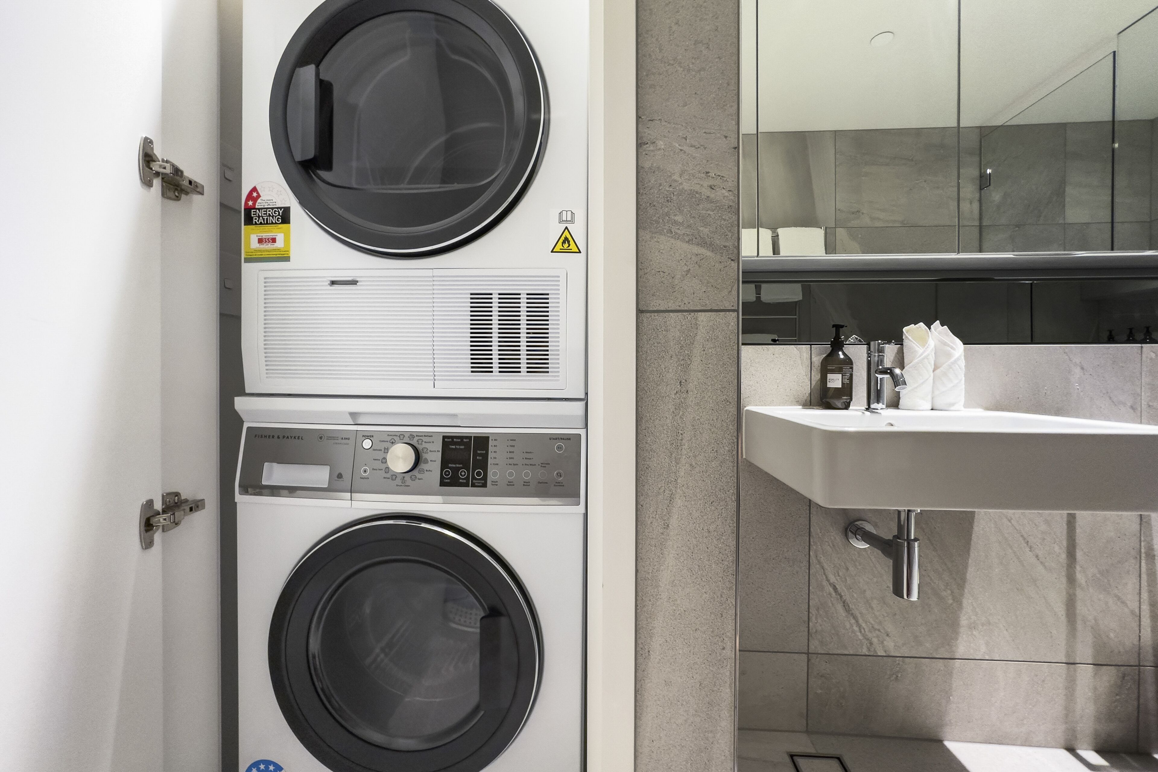 A laundry room with two stacked washing machines, a control panel, and a safety warning sign.
