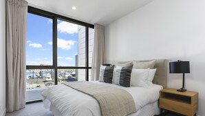 A modern hotel room with a large bed, a nightstand, and a view of the marina. - Modern tranquility in the city (Auckland)