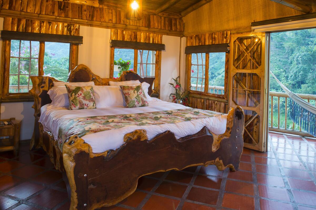A wooden bed with a floral bedspread in a room with large windows and a balcony.